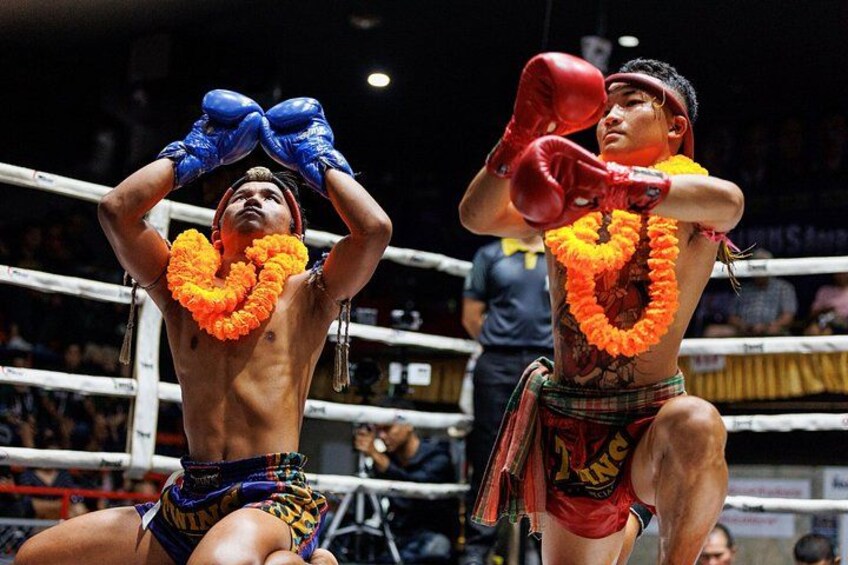 Zwei Boxer im Ring, einer mit blauen Handschuhen und der andere mit roten, beide mit orangefarbenen Girlanden um den Hals. 4