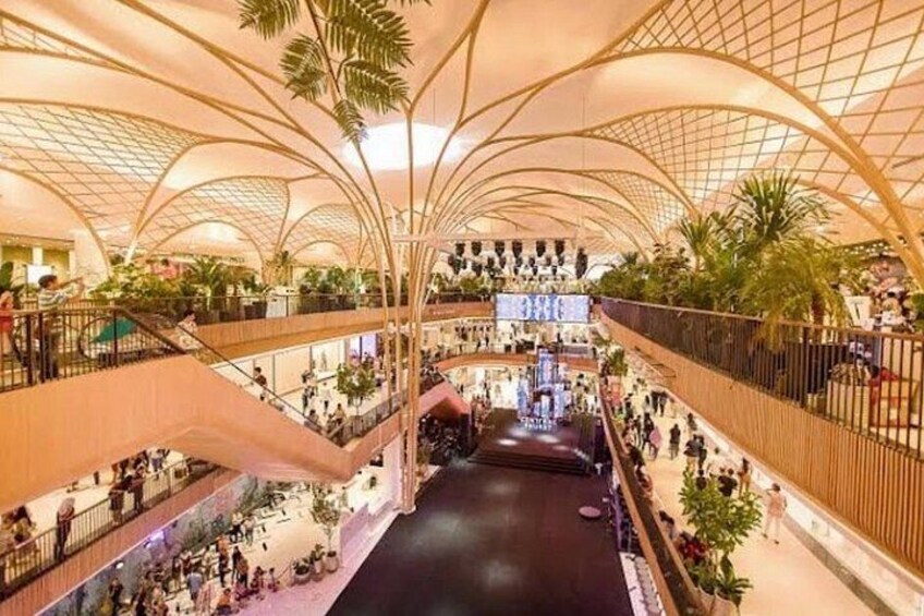 A multi-level shopping mall with curved ceilings, escalators, and indoor plants. 4