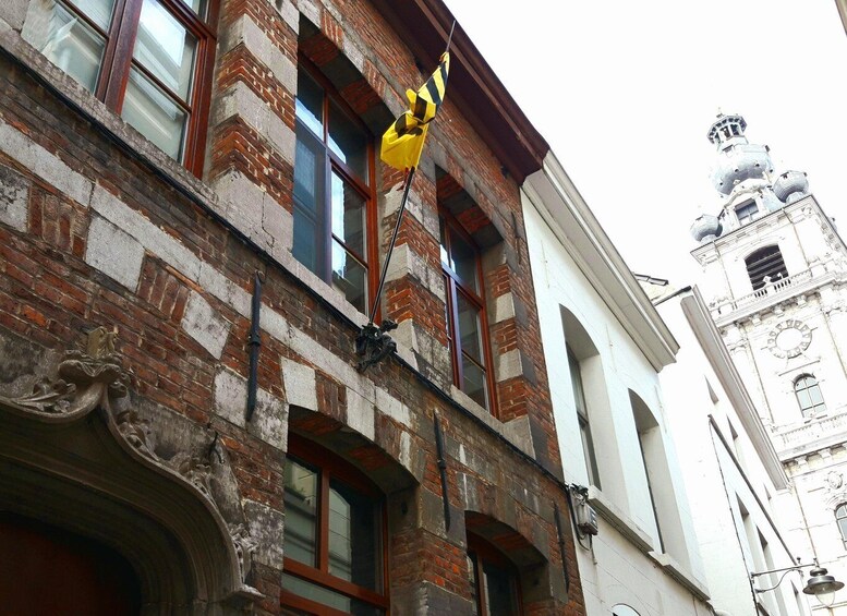 A historic building with a yellow flag, brickwork, and a clock tower in the background. 1