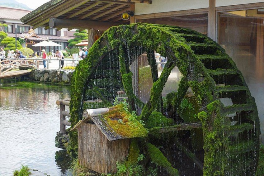 Una rueda de agua japonesa tradicional cubierta de musgo, una estructura de madera y un puente de piedra sobre un estanque. 3