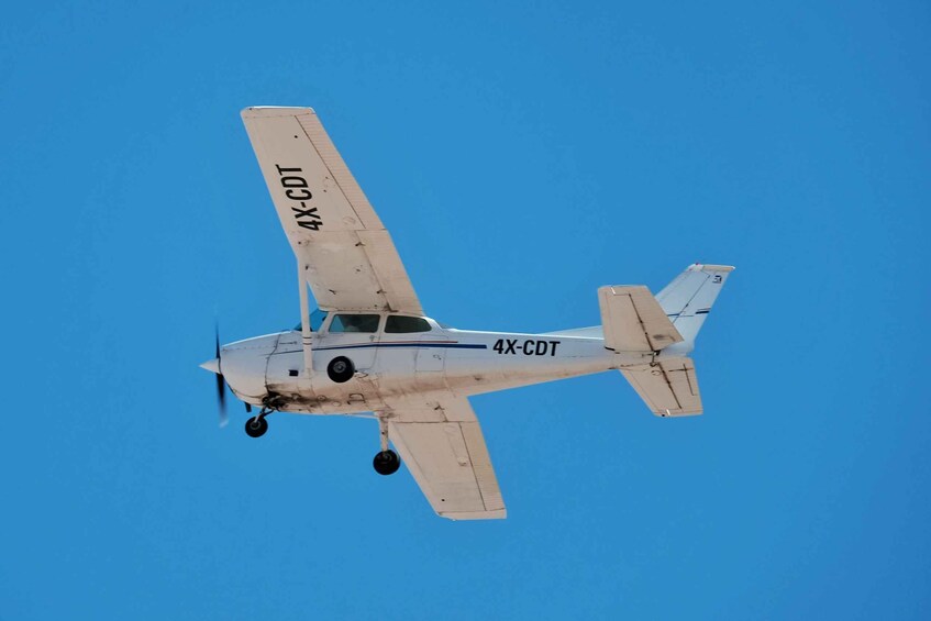 A small aircraft with the registration number 4X-CDT in flight against a clear blue sky. 5