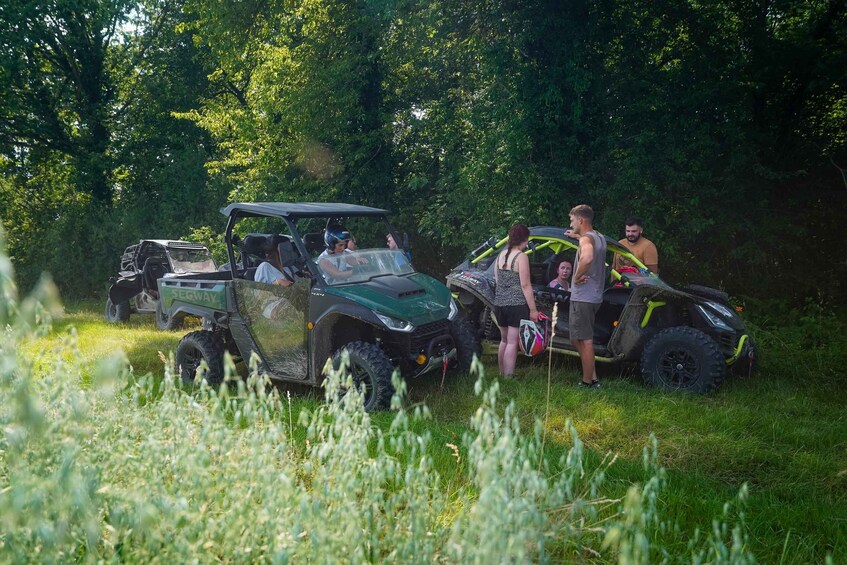 A group of people around off-road vehicles in a grassy area with trees in the background. 3