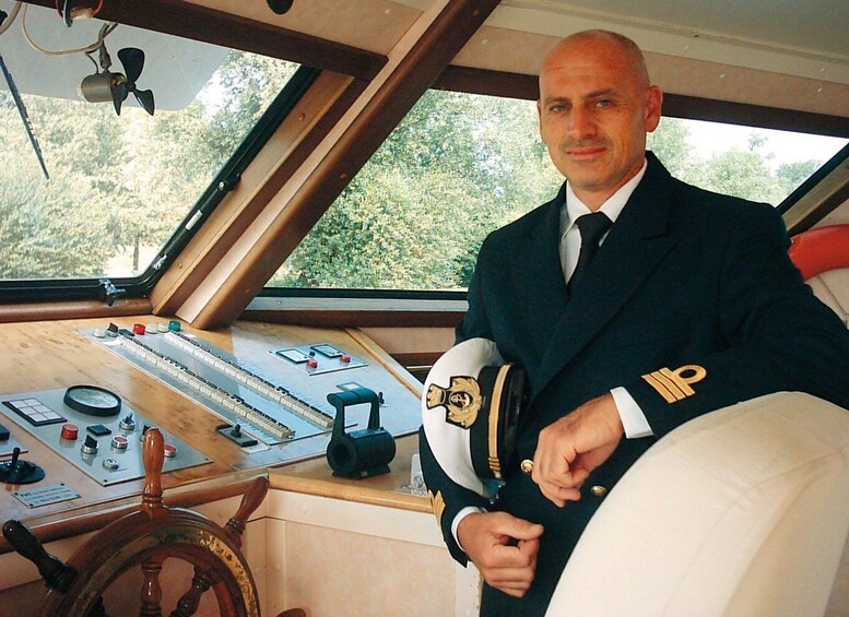 A man in a naval uniform standing in a ship's control room with various navigational instruments and a steering wheel. 2