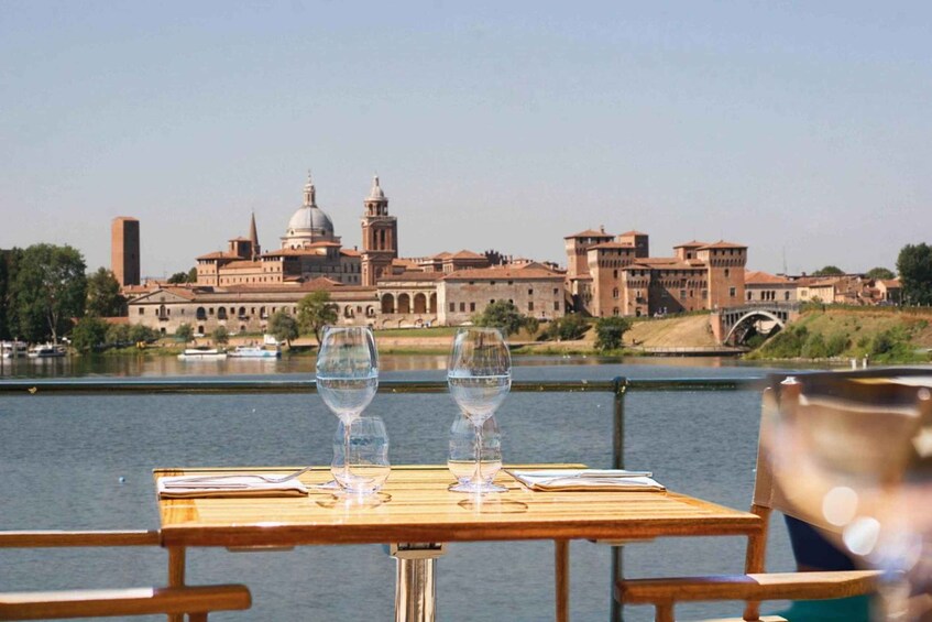 A table with two wine glasses and a menu, overlooking a historic building by a calm river. 3