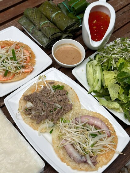 A variety of dishes including spring rolls, a salad, and a dish with shrimp and beef on a crispy base, served on a wooden table. 1