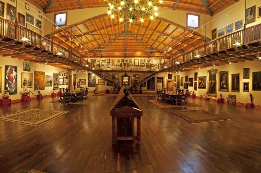 A spacious hall with wooden floors, a central piano, and artwork on the walls. 2