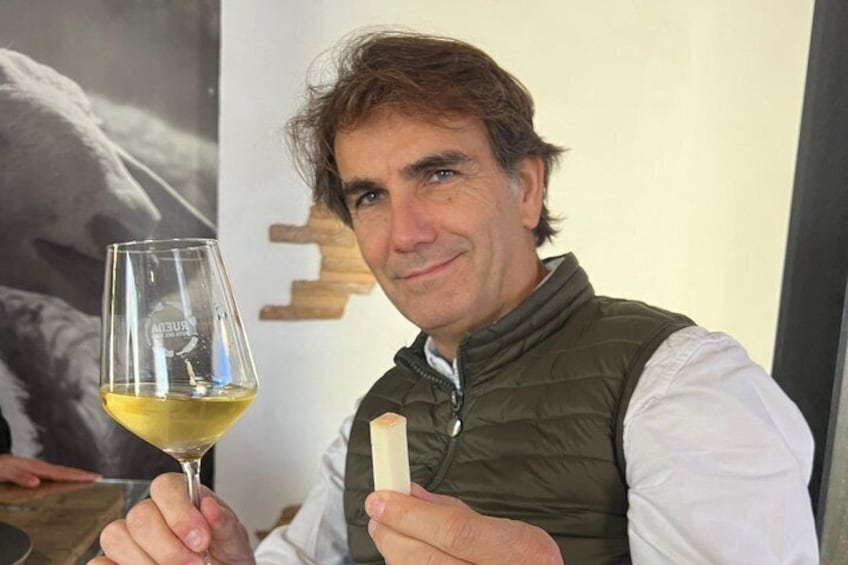 A person holding a wine glass and a small object, possibly a piece of food, with a poster in the background. 1