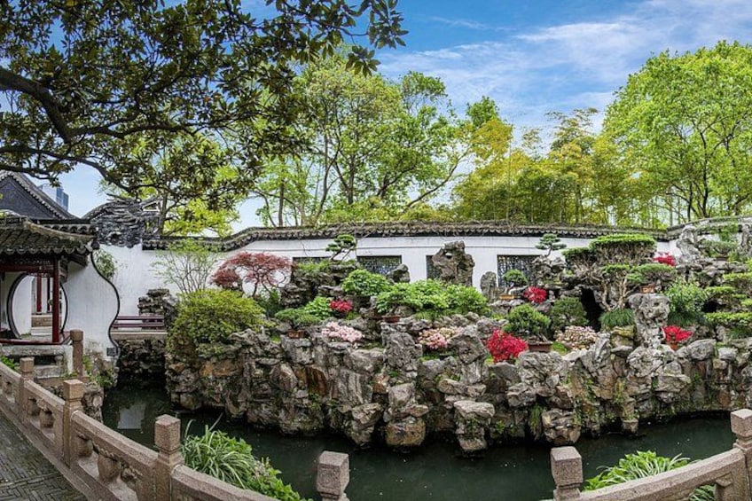 Un jardin chinois traditionnel avec un bassin rocheux, une végétation luxuriante et un bâtiment blanc doté d’un toit en tuiles. 5