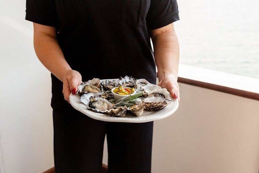A person holding a plate of oysters with lemon wedges and green onions. 4
