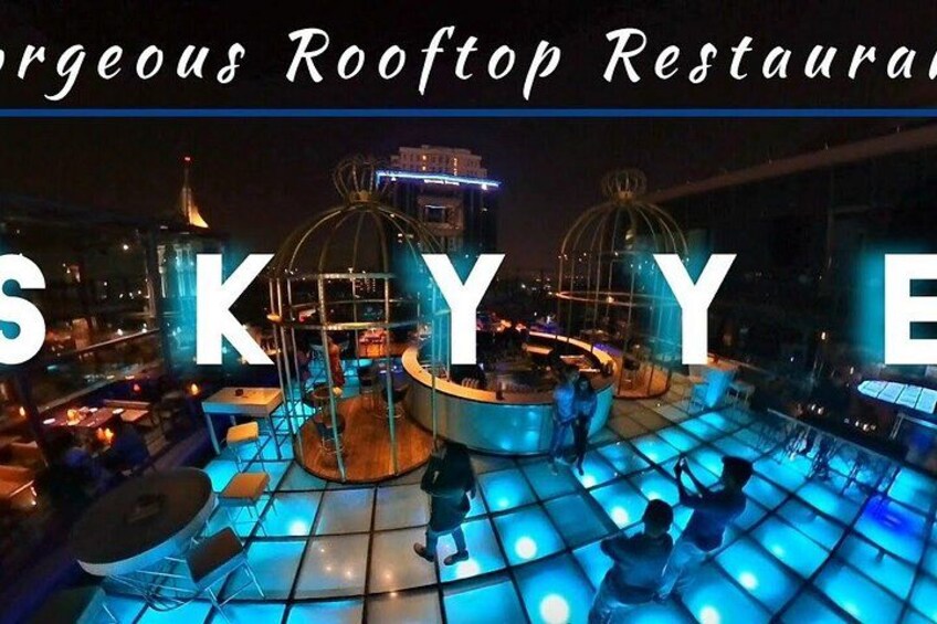 A rooftop restaurant with illuminated blue flooring, tables, and chairs, and a cityscape in the background. 5