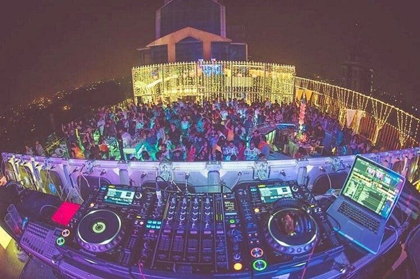 A DJ booth with multiple turntables and mixers, surrounded by a crowd at an outdoor event. 4