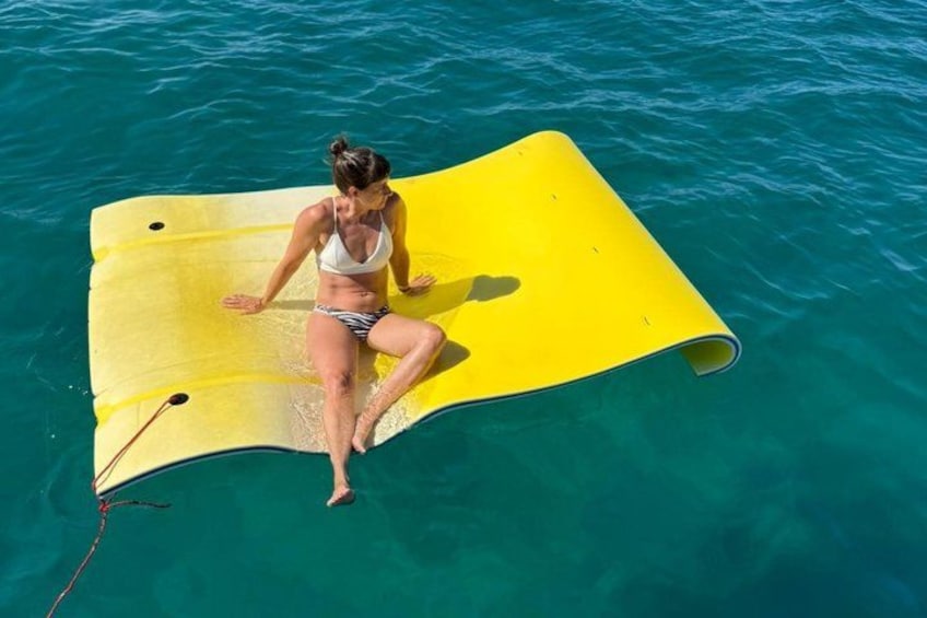 A person sitting on a yellow floating mat in clear blue water. 4