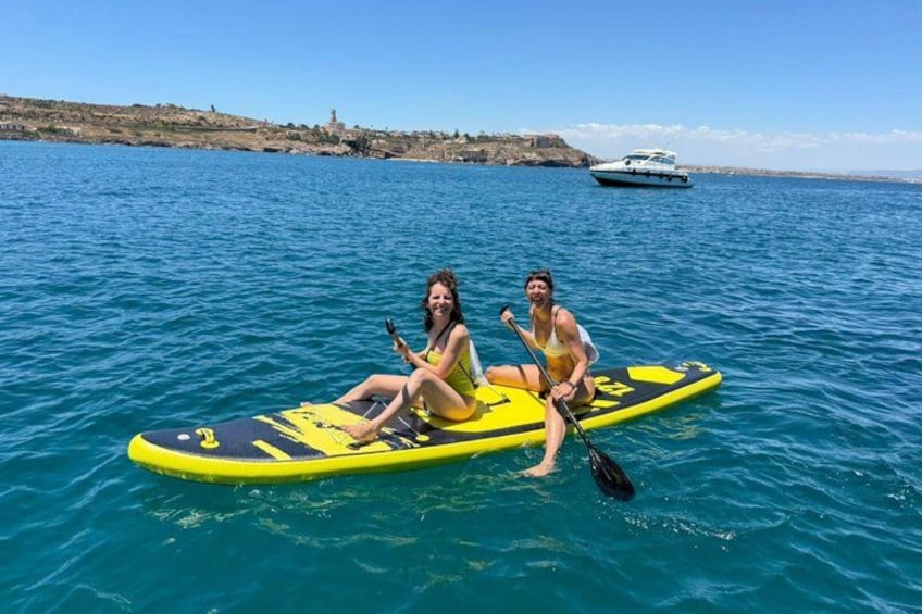 Two people on a yellow paddleboard in the water with a boat in the background. 2