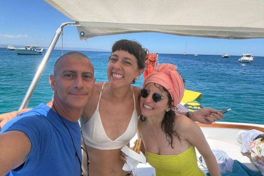 Three people on a boat with the sea and boats in the background. 3