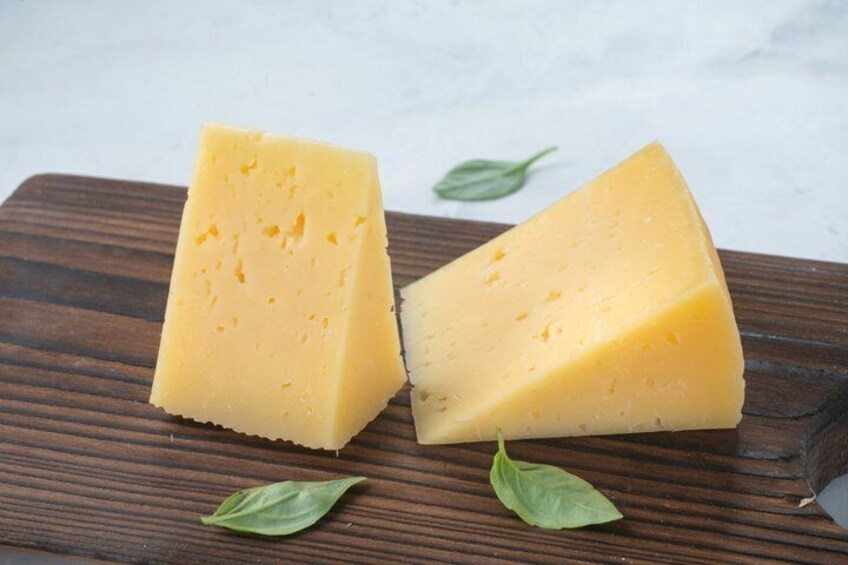 A wedge of cheese on a wooden board with a basil leaf. 2