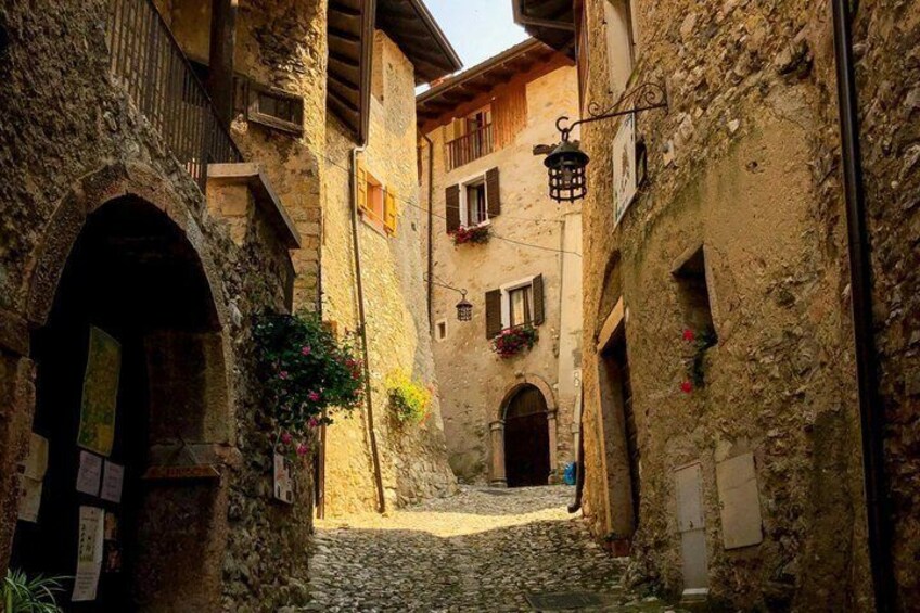 A narrow cobblestone street flanked by old stone buildings with arched doorways and wooden shutters. 5