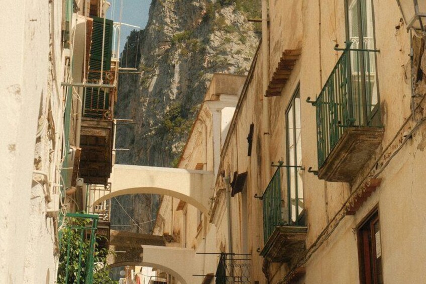 A narrow street with buildings, a stone bridge, and a rocky cliff in the background. 3