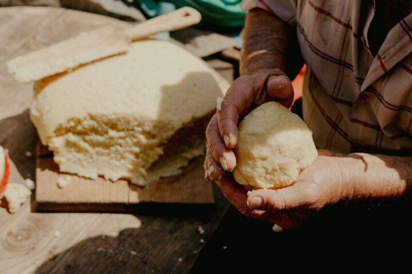 A person holding a piece of dough, with a wooden board and a rolling pin in the background. 1