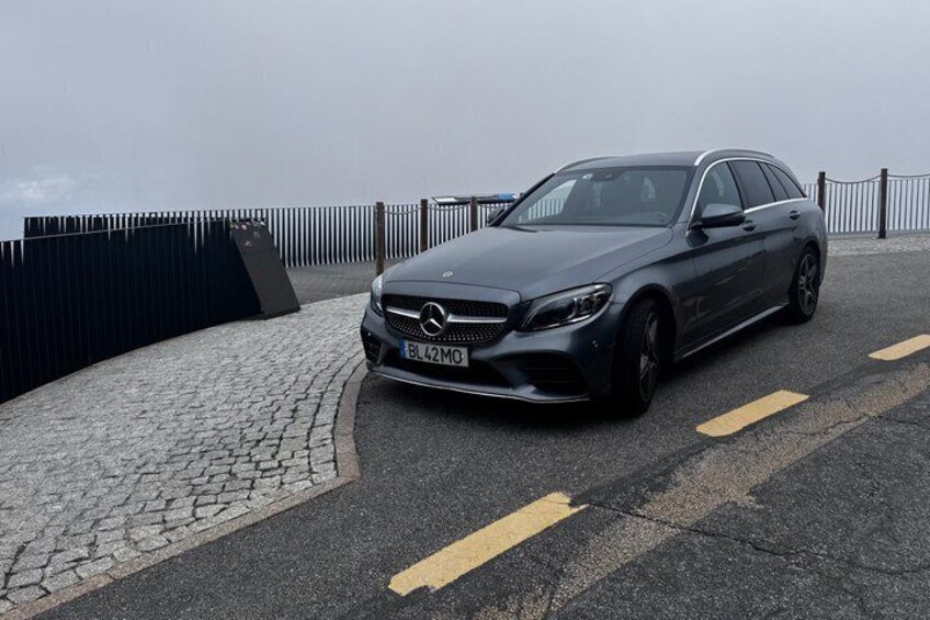 A dark-colored Mercedes-Benz parked on a paved area with a cobblestone path and a metal fence in the background. 5