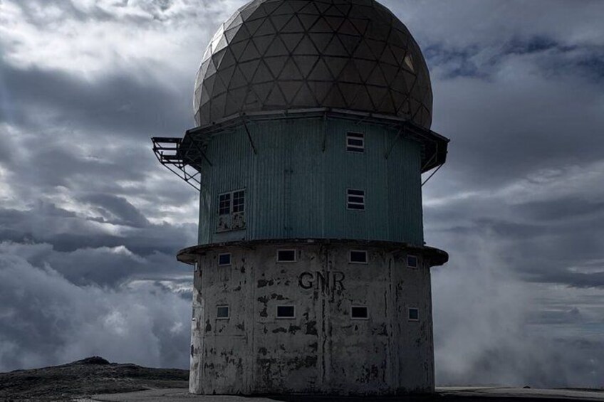 A weather radar station with a dome and a cylindrical base, surrounded by a cloudy sky. 4