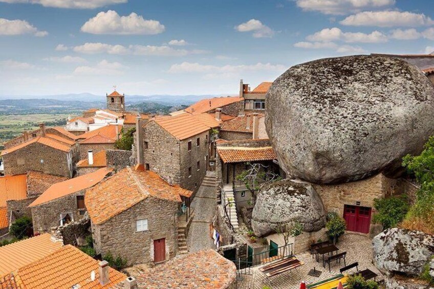 A village with stone buildings, a large rock, and a tower. 1