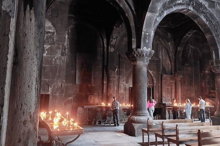 An interior of a historical building with stone arches, columns, and lit candles on the floor. 3