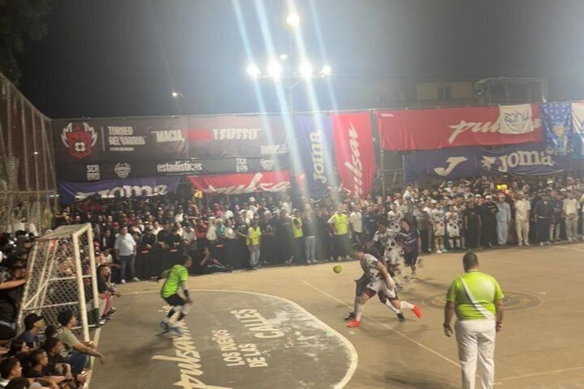 A nighttime soccer match with a crowd, goalposts, and a field marked with team names. 3