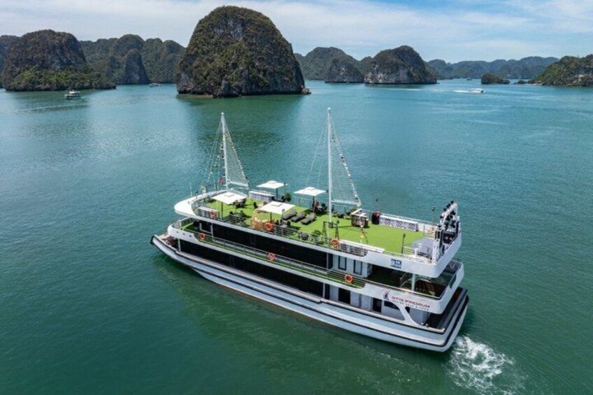 A large boat with a green deck, surrounded by calm water and limestone islands. 1