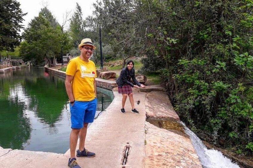 Un homme et une femme se tiennent sur un pont de béton qui enjambe une étendue d’eau, entourés de verdure. 2