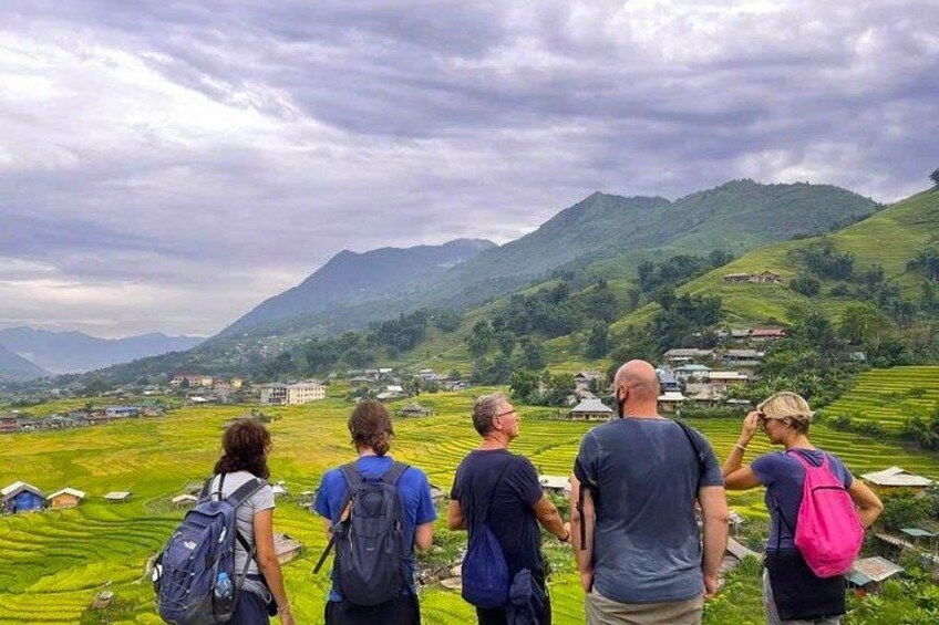 A group of people hiking on a mountain trail with lush green fields and a village in the background. 3