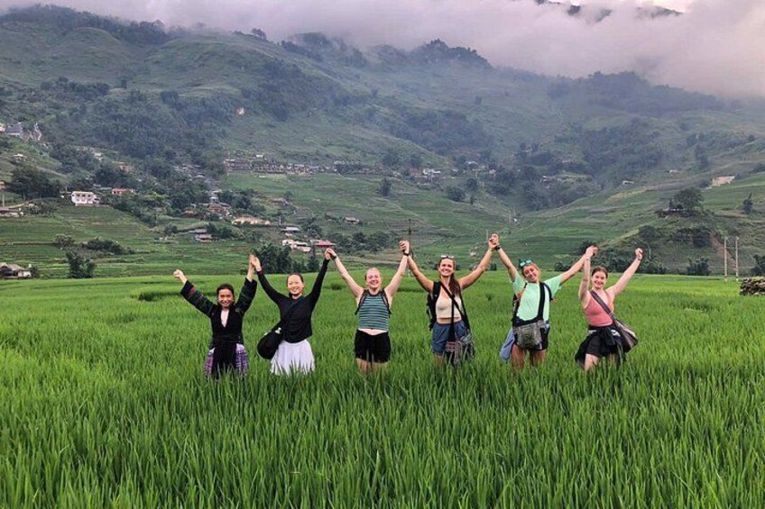 A group of people standing in a field with their arms raised, surrounded by green hills and a cloudy sky. 2