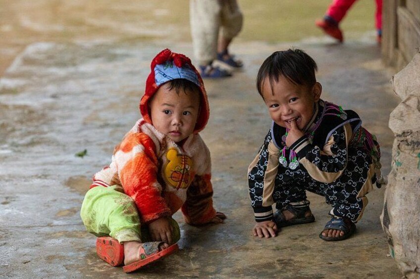 Two children sitting on a concrete floor, one wearing a red and white jacket and the other in a patterned outfit. 5