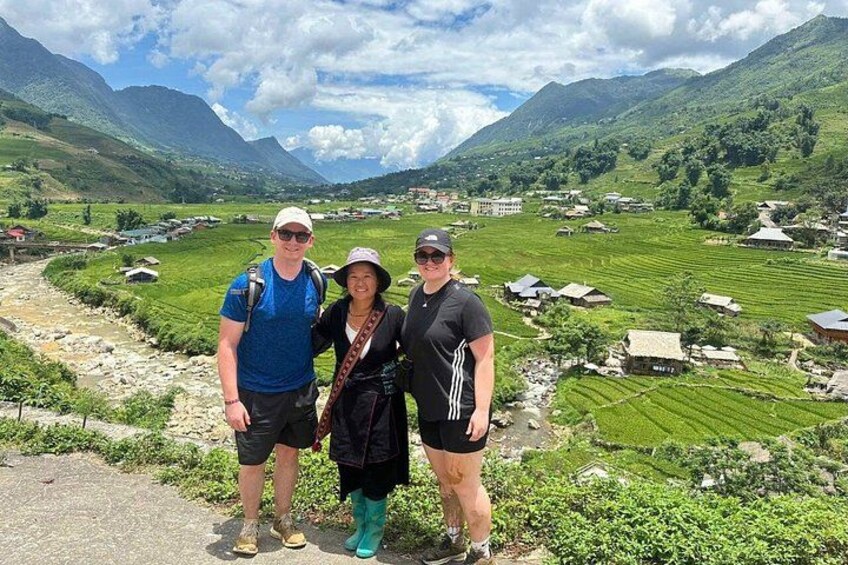 Three people standing on a path with a mountainous landscape and terraced fields in the background. 4
