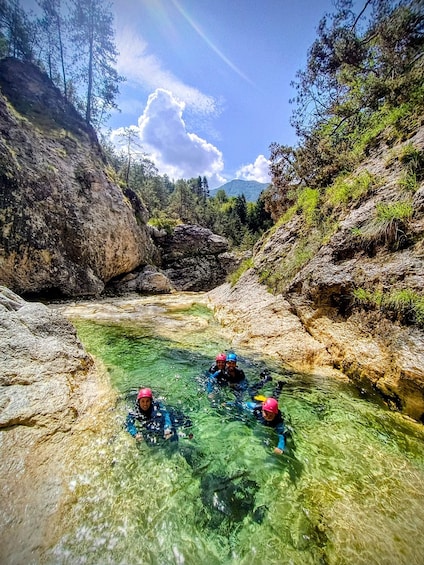 A group of people kayaking in a clear river surrounded by rocky terrain and trees. 2