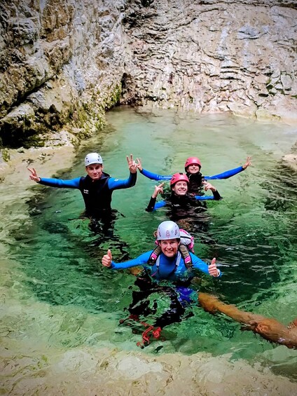 Four people in a river wearing helmets and life jackets, giving thumbs up. 3