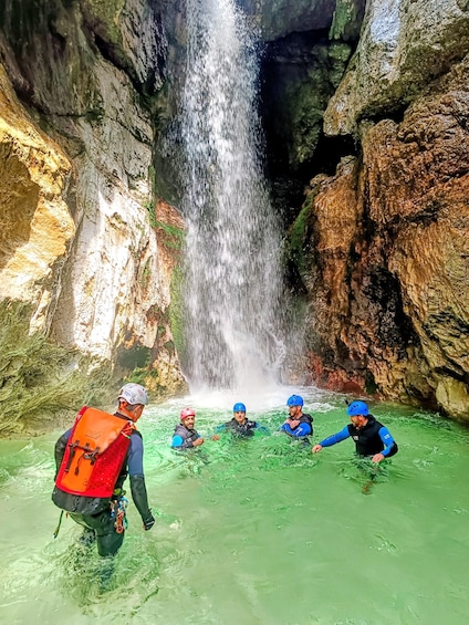 A group of people in water with a waterfall in a rocky cave. 1