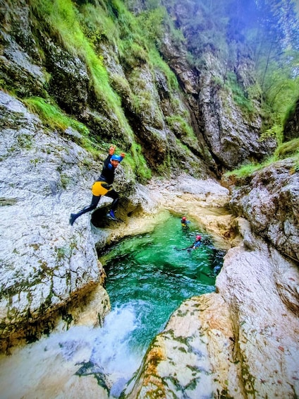 A person rappelling down a rocky cliff into a clear blue pool. 4