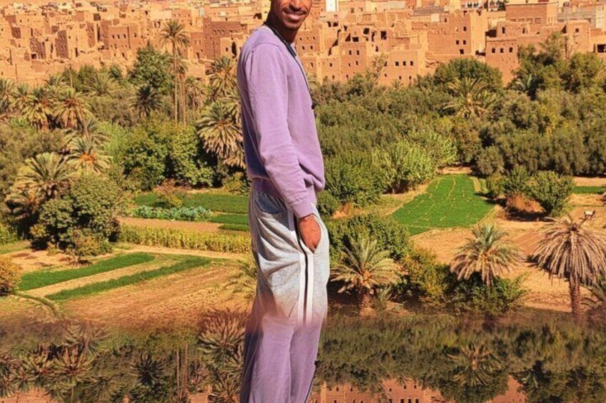 A person standing in a rural landscape with terraced fields and traditional buildings in the background. 4