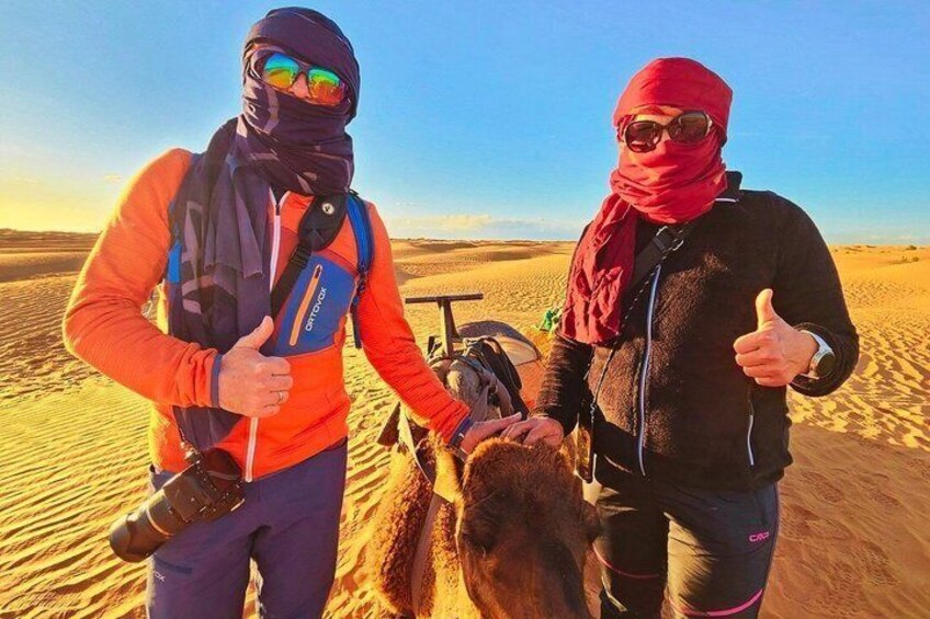 Two people in outdoor gear with a camel in a desert landscape. 1