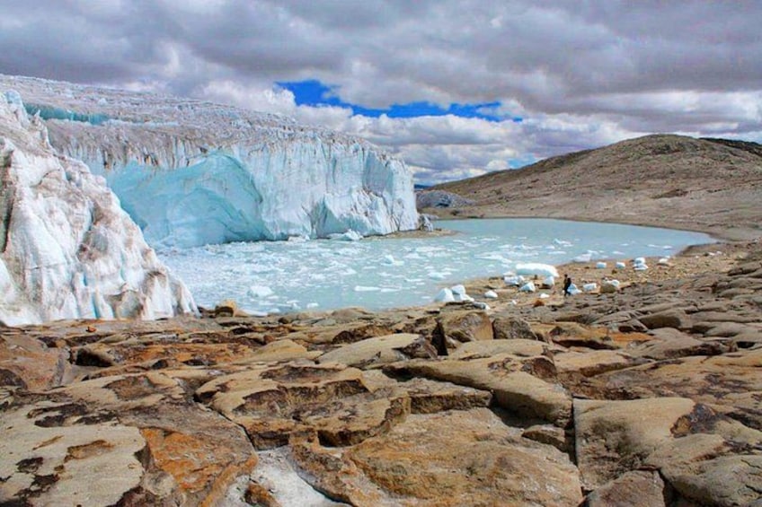 Un glaciar con una pared de hielo azul, un primer plano rocoso y un cielo nublado. 1