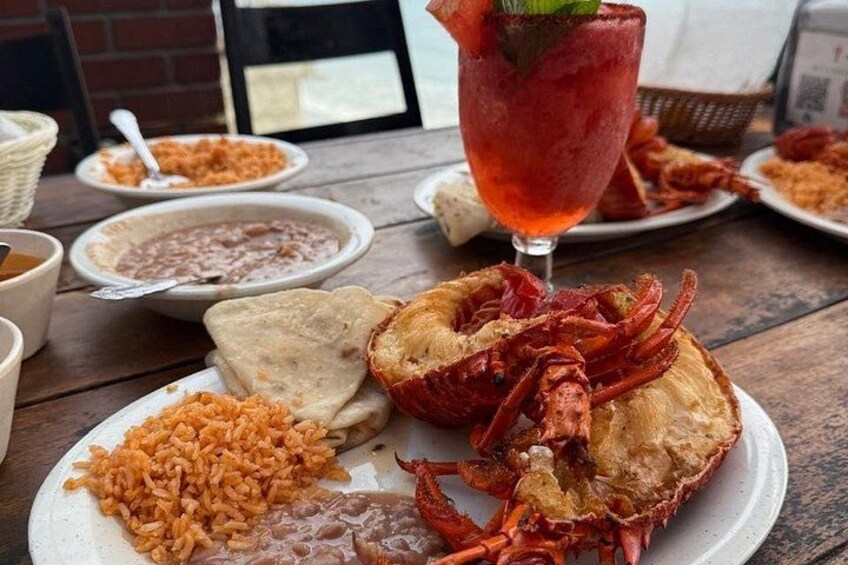 A meal with a lobster, rice, beans, and a drink on a wooden table. 2