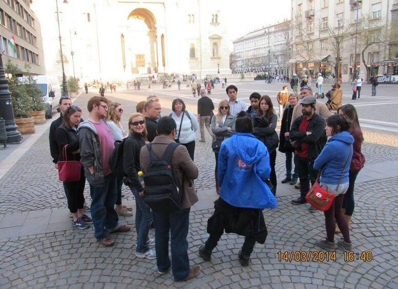 A group of people standing in a public square with historic architecture in the background. 3