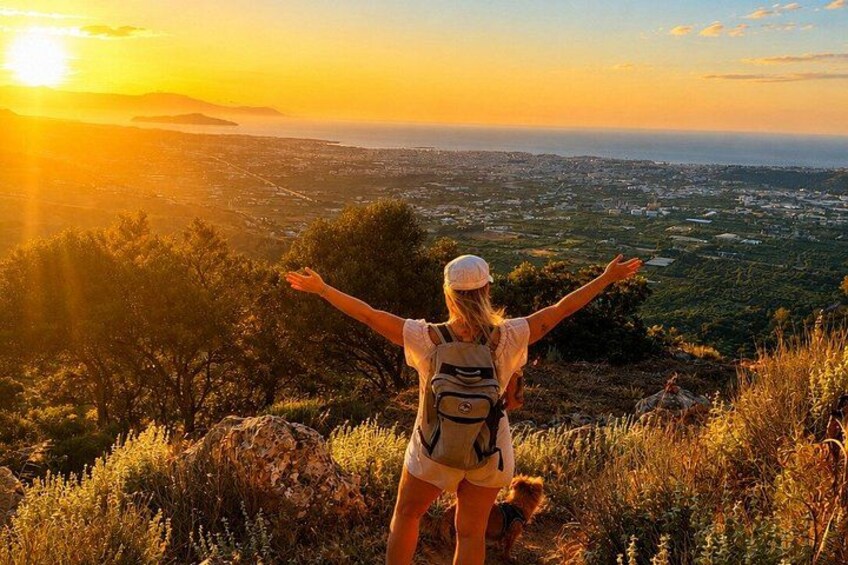 A person with arms outstretched on a hill overlooking a cityscape at sunset. 1