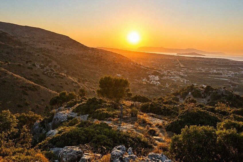 A sunset over a hilly landscape with scattered trees and a clear view of a distant town. 2