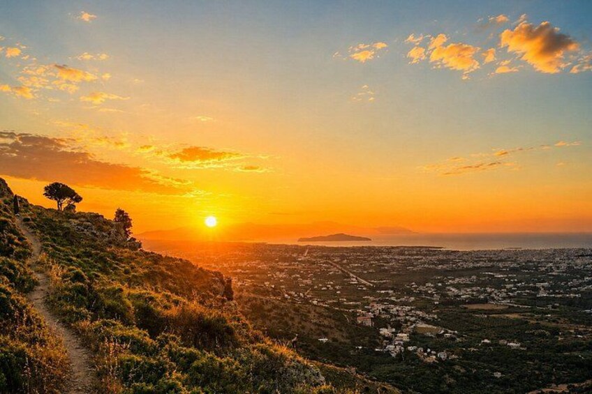 A sunset over a hilly landscape with a path and scattered trees. 3