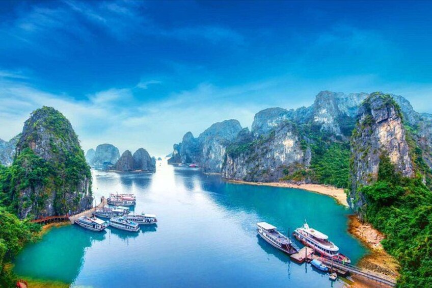 A coastal area with boats docked, a clear blue sea, and limestone karsts. 1