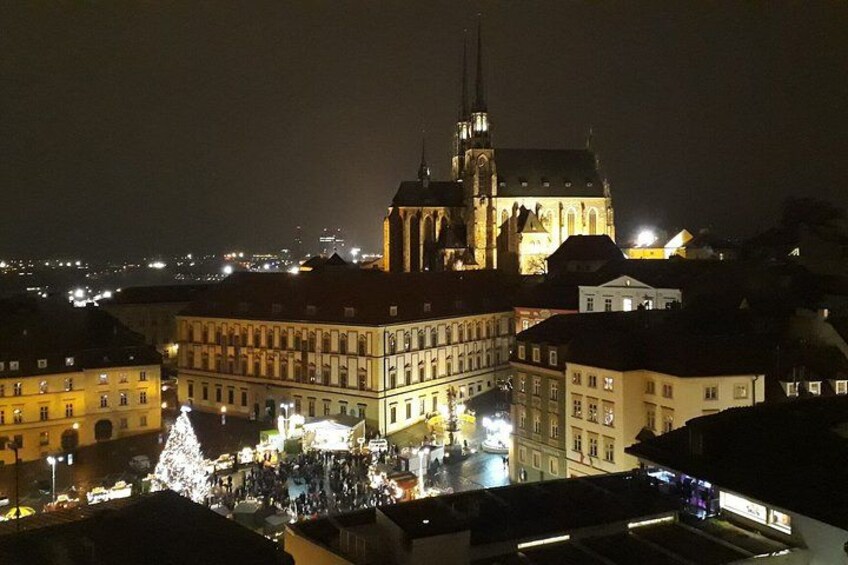 A cityscape at night with illuminated buildings, a prominent church with a spire, and a decorated Christmas tree. 1