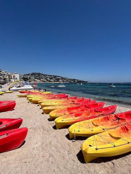 A beach with rows of colorful kayaks lined up on the sand, a clear blue sky, and a calm sea with boats in the background. 1