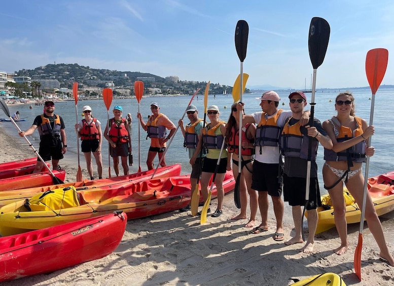 A group of people standing on a beach with kayaks and paddles, wearing life jackets. 2
