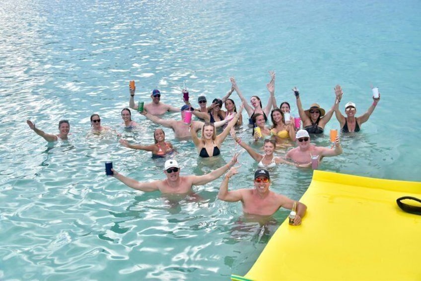 Un grupo de personas en el agua, algunas sosteniendo bebidas, con un objeto amarillo a la derecha. 1
